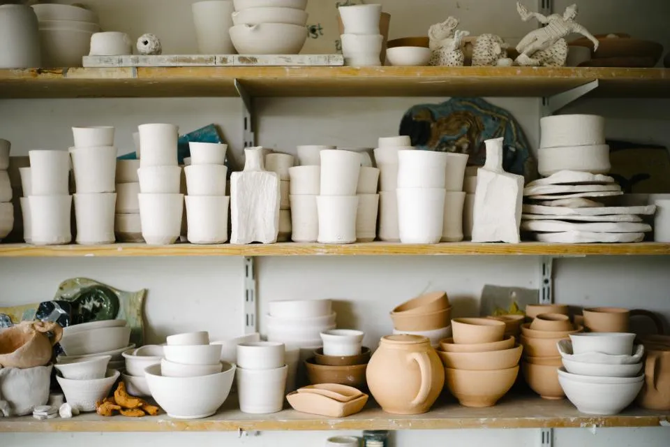 Workshop shelves stacked with thrown cups, bowls and jars before and after firing